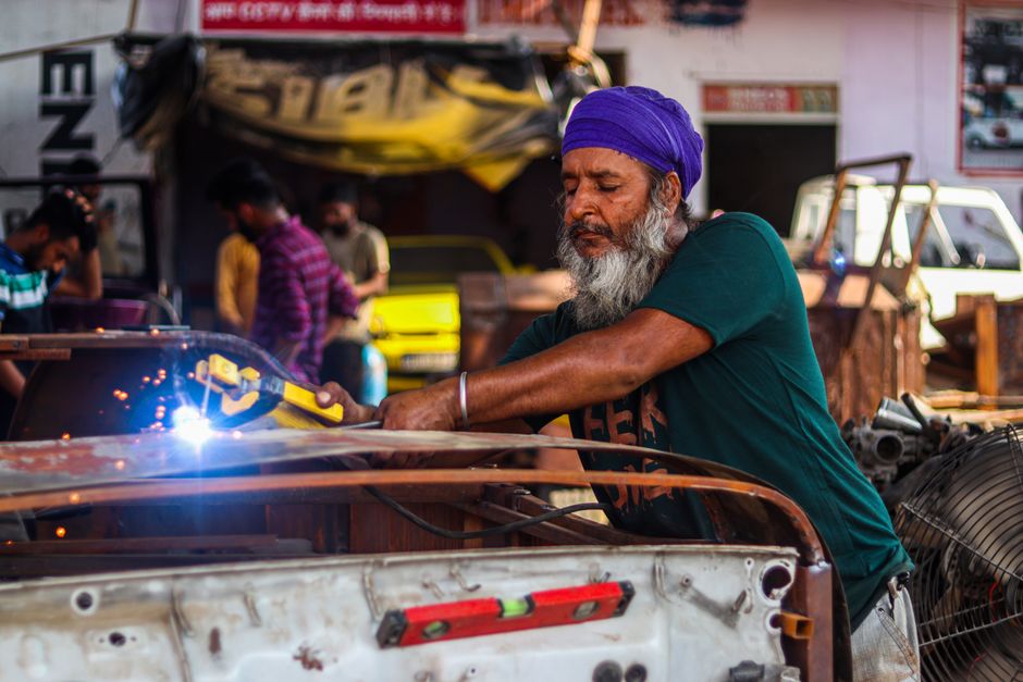 Man welding a car's metal frame in a busy workshop setting.